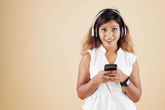 Retrato de mujer asiática joven emocionada disfrutando de su música favorita en auriculares y enviando mensajes de texto a amigos