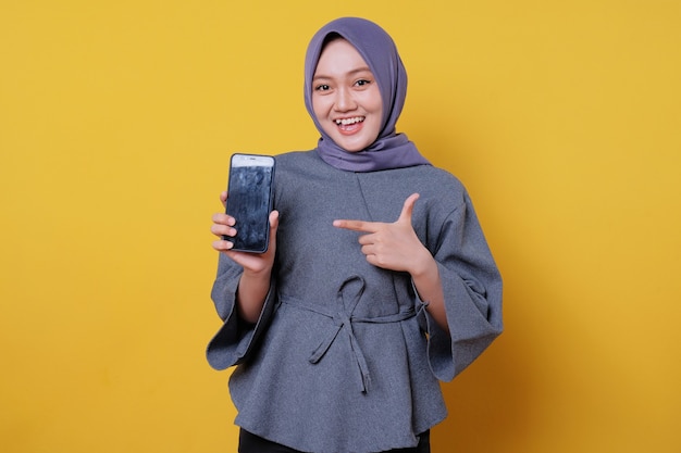 Retrato de una mujer asiática joven feliz celebrando con teléfono móvil aislado sobre fondo amarillo