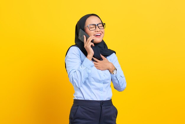 Retrato de mujer asiática joven feliz hablando por teléfono móvil aislado sobre fondo amarillo