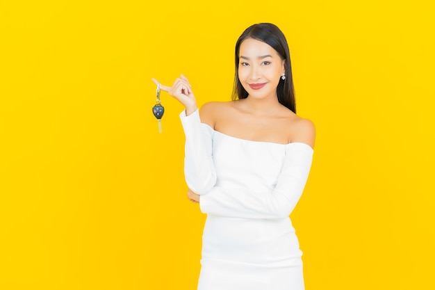 Retrato de mujer asiática joven hermosa con la llave del coche en la pared amarilla