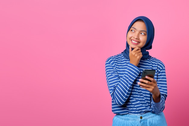 Retrato de mujer asiática joven pensando en pregunta con la mano en la barbilla mientras sostiene el teléfono inteligente