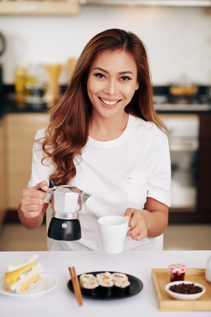 Retrato de mujer asiática joven positiva desayunando y una taza de café en casa