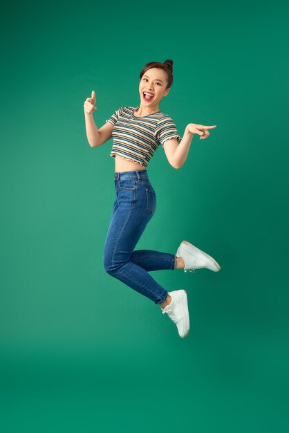 Retrato de mujer asiática joven positiva feliz saltando y agitando la mano sobre verde.