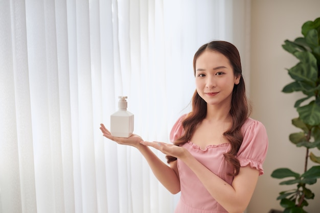 Retrato de mujer asiática joven que muestra el nuevo producto mientras está de pie detrás de la ventana.