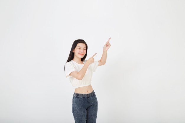 Retrato de mujer asiática joven sonriente con camiseta de verano apuntando al espacio de la copia con un dedo