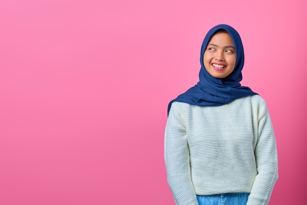 Retrato de mujer asiática joven sonriente mirando a otro lado al lado sobre fondo rosa