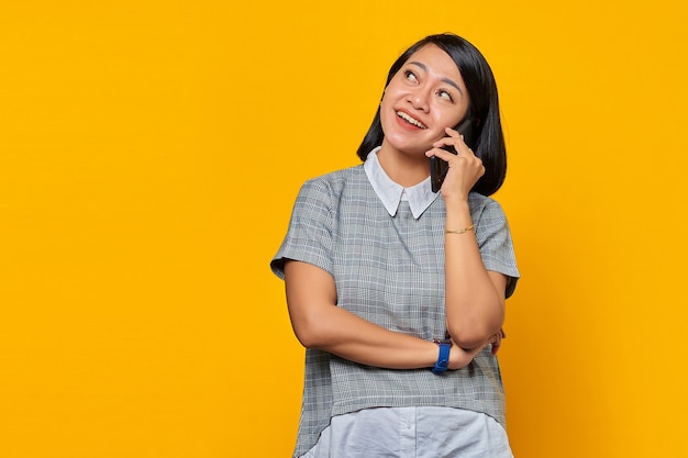 Retrato de mujer asiática joven sonriente que recibe la llamada entrante en el teléfono inteligente y mirando a un lado