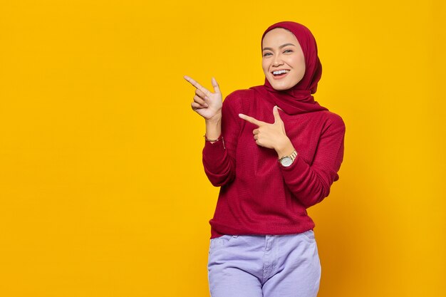 Retrato de mujer asiática joven sonriente que señala el dedo en el espacio de la copia sobre fondo amarillo