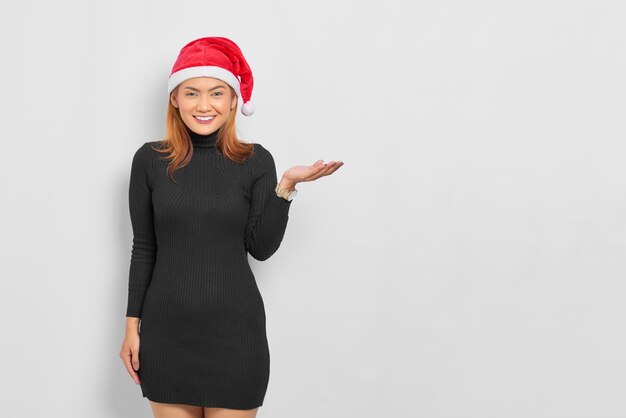 Retrato de mujer asiática joven sonriente con sombrero de Santa Claus mostrando copia espacio en la palma aislado sobre fondo blanco.