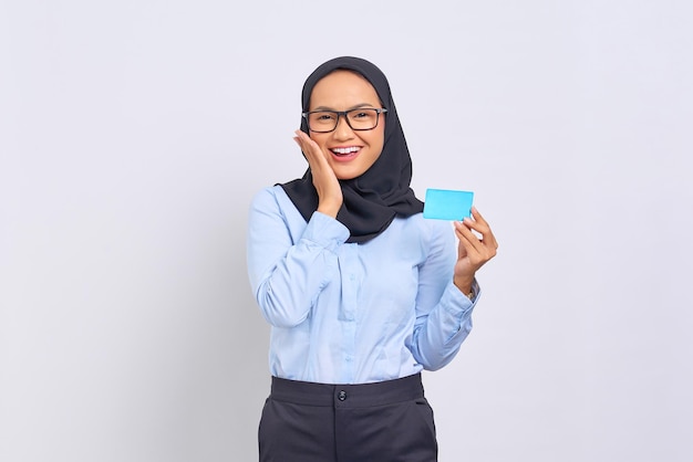 Retrato de mujer asiática joven sonriente tocando la mejilla de la cara, sosteniendo la tarjeta de crédito aislado sobre fondo blanco.