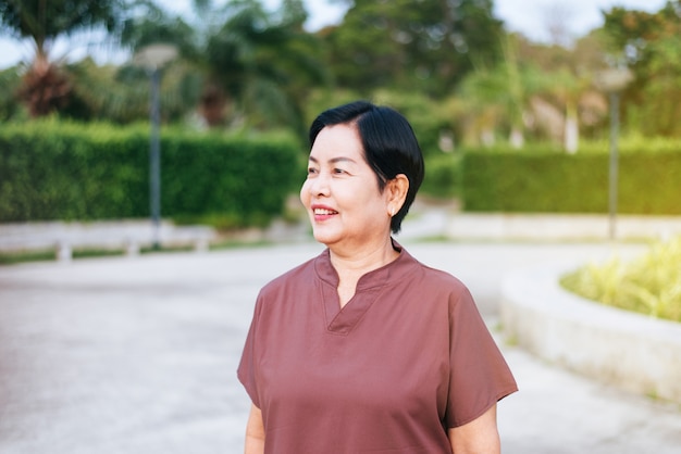 Retrato de mujer asiática madura de pie en el parque público, feliz y sonriente, concepto de seguro de cuidado superior