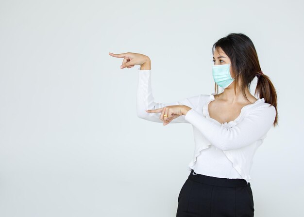 Retrato de mujer asiática con una máscara facial plantea, señalando publicidad sobre fondo blanco, espacio de copia en blanco con recorte de fondo blanco aislado.