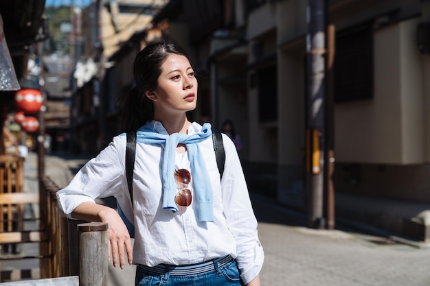 retrato de una mujer asiática mirando a la distancia en contemplación mientras descansa su brazo en el pasamanos de madera en la calle hanamikoji en gion, japón en un día soleado