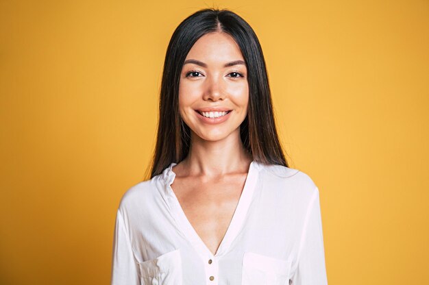 Retrato de mujer asiática morena joven feliz sobre fondo amarillo