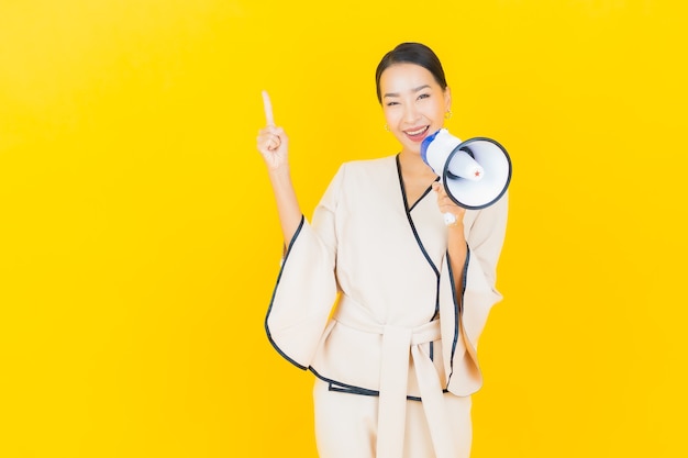Retrato de mujer asiática de negocios joven hermosa con megáfono para comunicación en pared amarilla