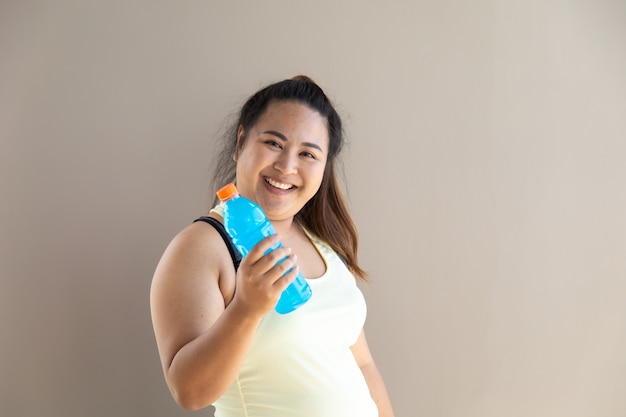 Retrato de mujer asiática con sobrepeso en ropa deportiva sosteniendo una botella de agua
