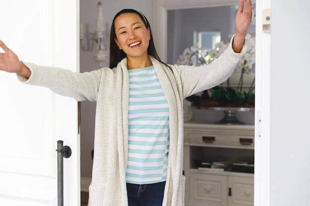 Retrato de una mujer asiática sonriente con los brazos abiertos saludando al visitante en la puerta