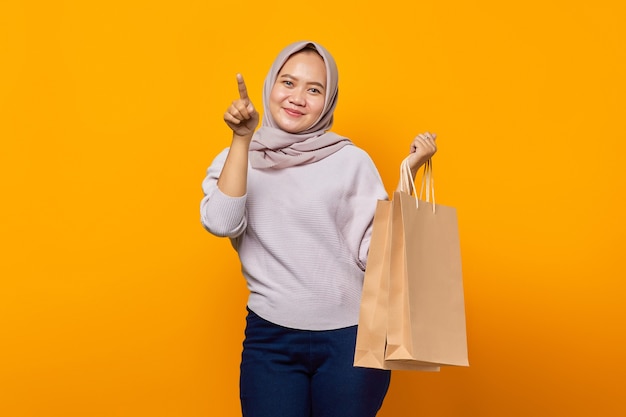 Retrato de mujer asiática sonriente sosteniendo bolsa de compras y señalando con el dedo en el espacio vacío