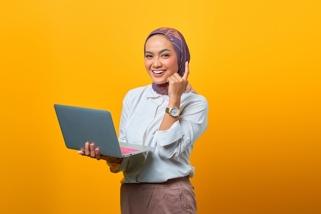 Retrato de mujer asiática sonriente sosteniendo portátil tiene buenas ideas sobre fondo amarillo