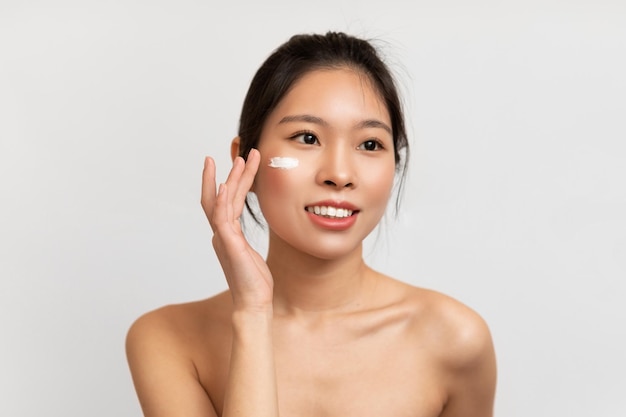 Retrato de mujer asiática tocando aplicar crema en las mejillas