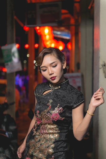 Retrato de una mujer asiática vestida de negro en la pasarela en la escena nocturna del centro de la ciudad cierra el estilo callejero de una chica