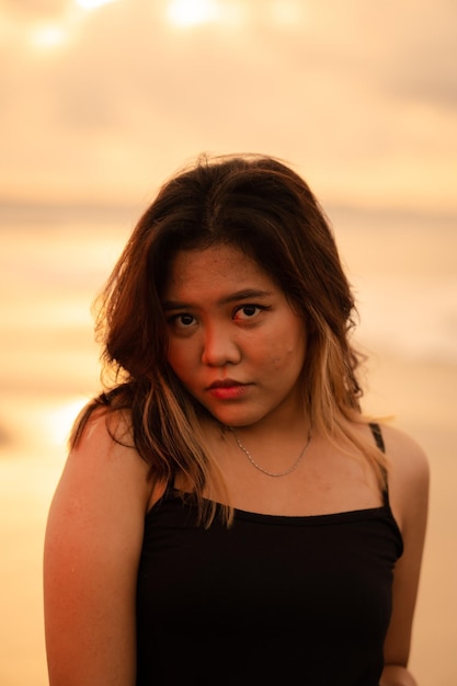 Un retrato de una mujer asiática con un vestido negro haciendo una pose sexy mientras disfruta de la vista cerca de la playa