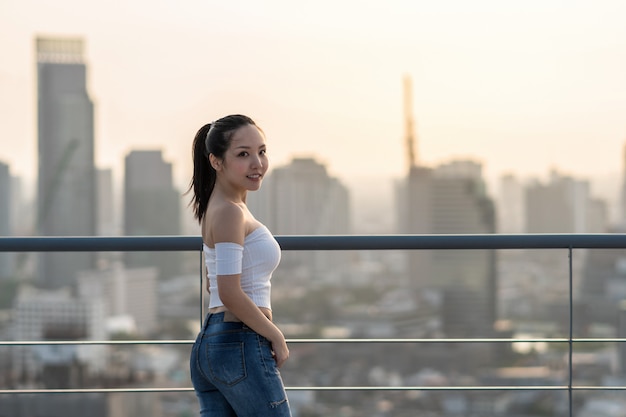 Retrato de mujer asiática de Yong en traje de moda sexy de pie en la azotea sobre el paisaje urbano