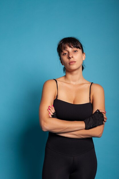 Retrato de mujer atlética en ropa deportiva de pie en estudio con fondo azul durante el entrenamiento deportivo. Entrenador personal estirando los músculos del cuerpo practicando ejercicios trabajando en un estilo de vida saludable