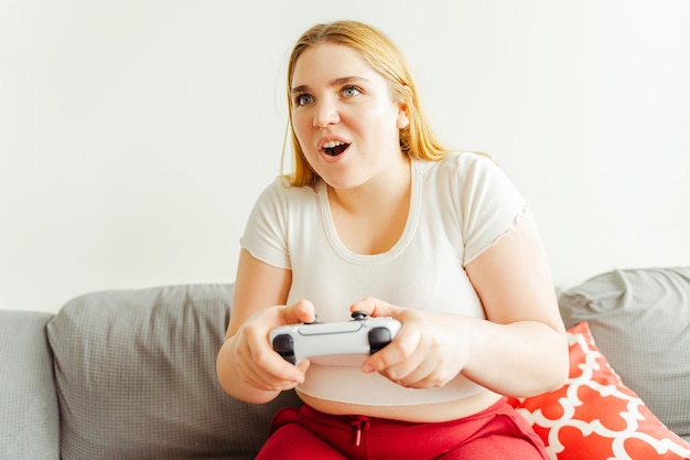 Retrato de una mujer atractiva con un cuerpo positivo en un cómodo sofá en un apartamento jugando videojuegos Mujer elegante con ropa casual divirtiéndose en línea Concepto tecnológico