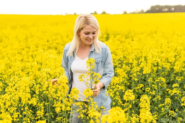 Retrato de una mujer atractiva en un floreciente campo de colza con luz de puesta de sol. Flores amarillas y mujer feliz.