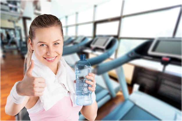 Retrato de mujer atractiva joven alegre mostrando gesto de pulgares arriba, con botella de agua,