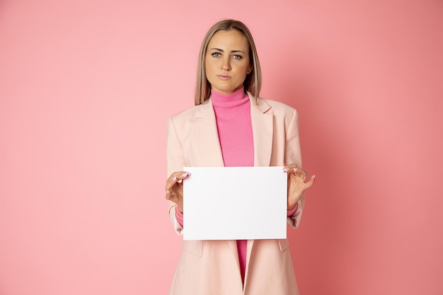 Retrato de mujer atractiva joven de pelo rubio de 30-35 años sosteniendo el espacio en blanco de papel A4 para firmar sobre fondo rosa. La empresaria lleva una chaqueta rosa. Directora superior, blog femenina