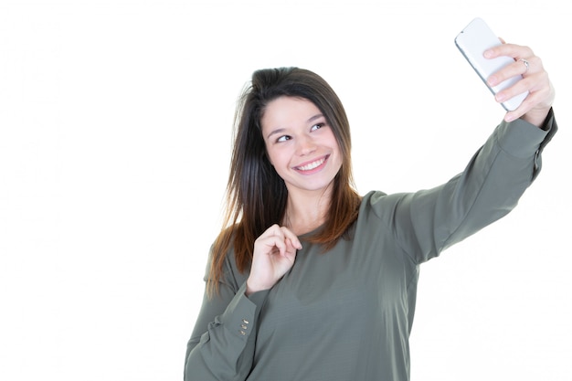 Foto retrato de una mujer atractiva joven que hace la foto del selfie con smartphone en el fondo blanco