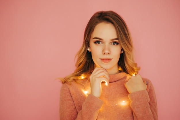 retrato de mujer atractiva en luces de Navidad aislado sobre fondo de color rosa mirando a la cámara