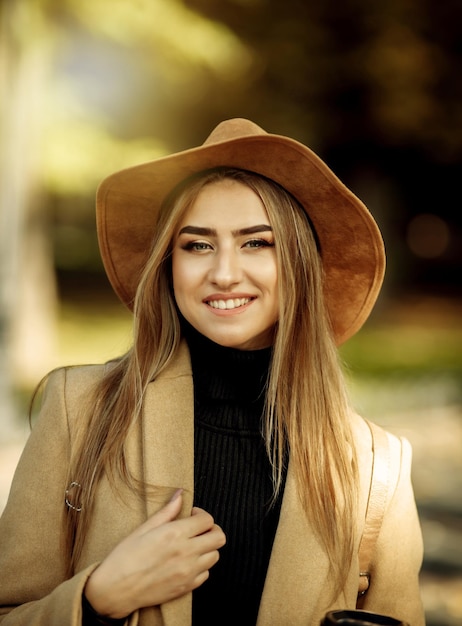 Retrato de una mujer atractiva con maquillaje vestida con un abrigo y un sombrero de fieltro. Paseo en el parque de la ciudad de otoño