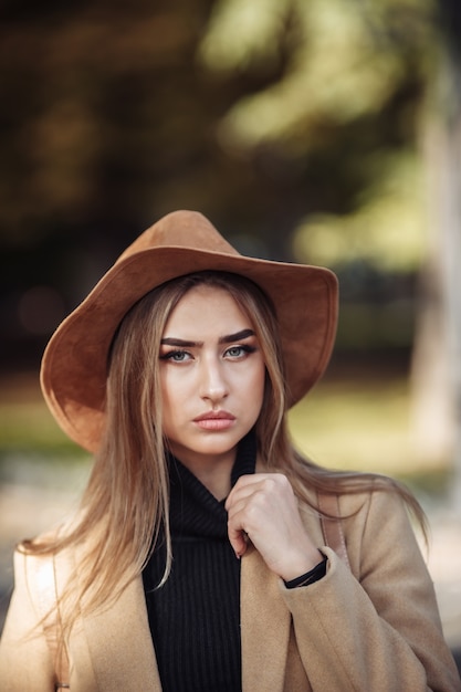 Retrato de una mujer atractiva con maquillaje vestida con un abrigo y sombrero de fieltro.