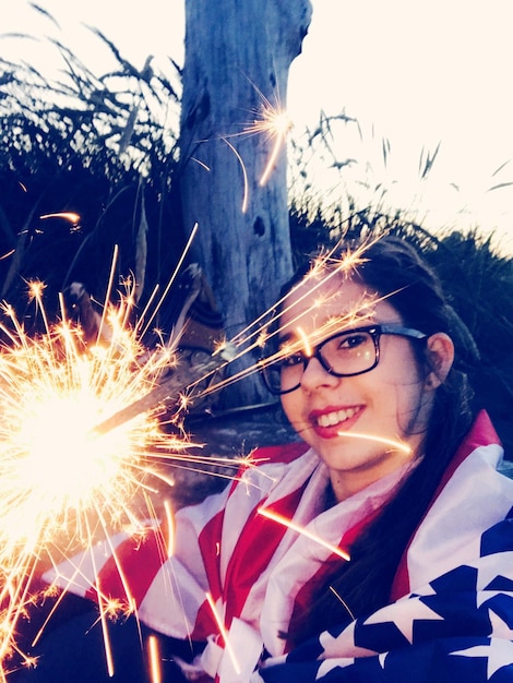 Foto retrato de una mujer con una bandera estadounidense sosteniendo una chispa iluminada