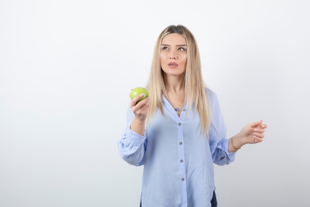 Retrato de una mujer bastante atractiva modelo de pie y sosteniendo una manzana verde fresca.