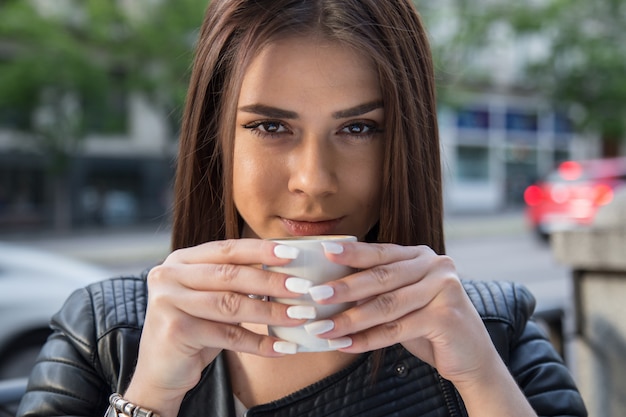 Retrato de mujer bastante caucásica tomando café en una terraza en la calle.