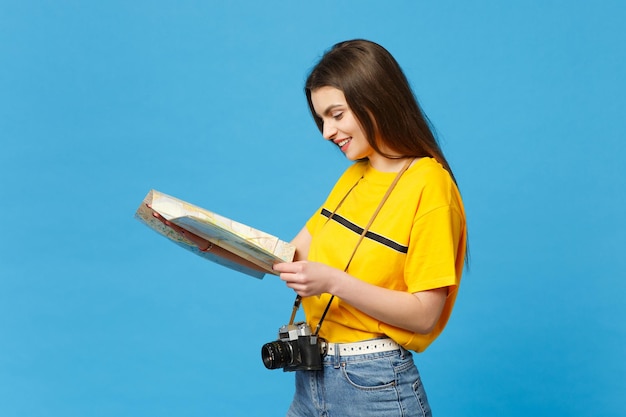 Retrato de una mujer bastante joven con ropa informal vívida con una cámara de fotos retro vintage sosteniendo un mapa de la ciudad de papel aislado en el fondo de la pared azul en el estudio. Concepto de estilo de vida de las personas. Simulacros de espacio de copia.