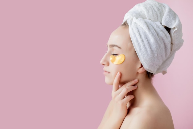 Retrato de mujer de belleza con parches en los ojos sobre fondo rosa Cara de belleza de mujer con máscara debajo de los ojos Hermosa mujer con maquillaje natural y cosméticos dorados Parches de colágeno en piel facial fresca