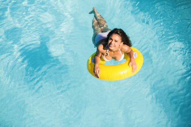 Retrato de mujer en bikini blanco flotando en un tubo inflable en la piscina