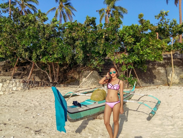 Foto retrato de una mujer en bikini de pie en la playa contra los árboles