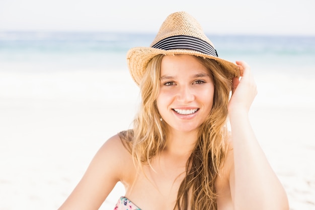 Retrato de mujer bonita en bikini y sombrero sentado en la playa