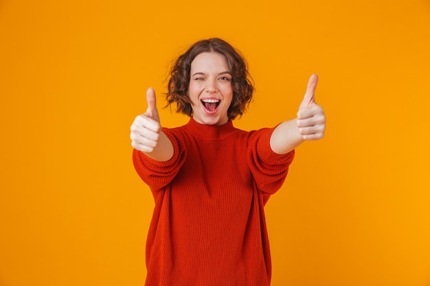 Retrato de una mujer bonita joven feliz posando aislada sobre pared amarilla mostrando los pulgares para arriba.