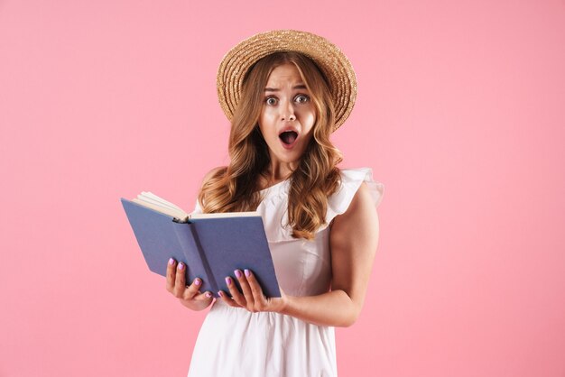 Retrato de una mujer bonita joven linda confundida sorprendida posando aislada sobre el libro de lectura de la pared rosa. Mirando la cámara.