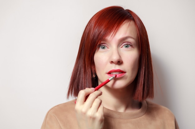 Retrato de mujer bonita pelirroja pinta sus labios con lápiz labial rojo