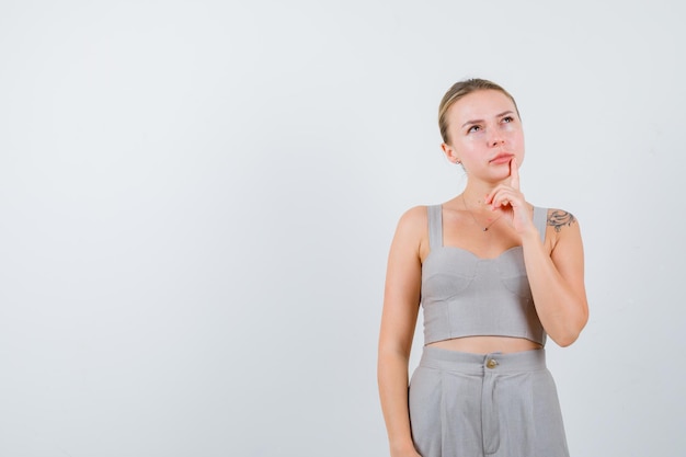 Retrato de mujer bonita puso el dedo en la boca en traje gris escotado con tatuaje y mirando pensativo