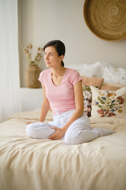 Retrato de mujer bonita en ropa casual sentada en la cama en casa