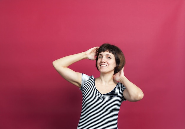 Retrato de mujer bonita de treinta años con pelo corto en vestido de rayas sobre fondo rosa